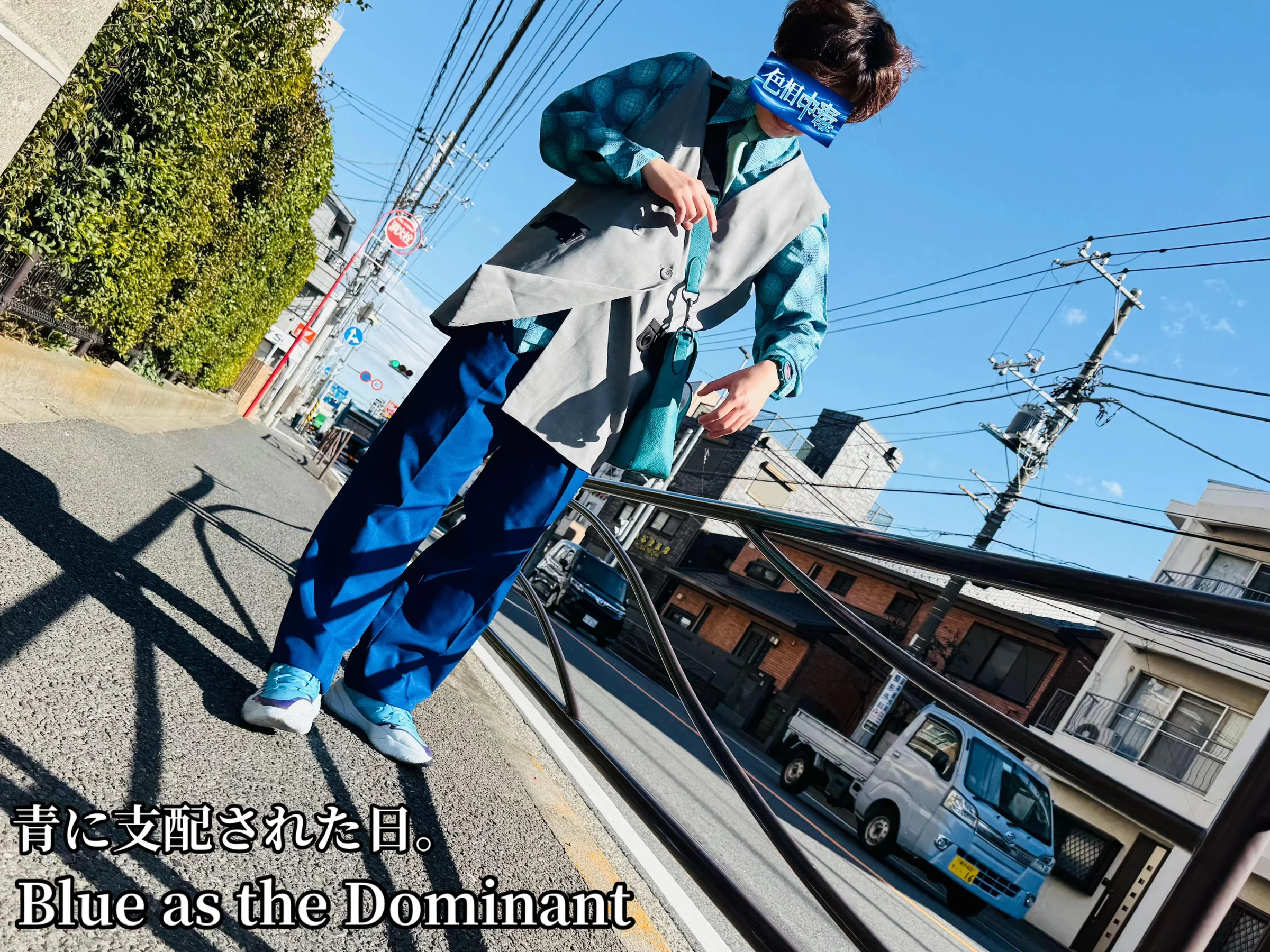 青緑の柄シャツ、グレーのベスト、鮮やかな青いパンツを着て川崎の街角に立つ人物