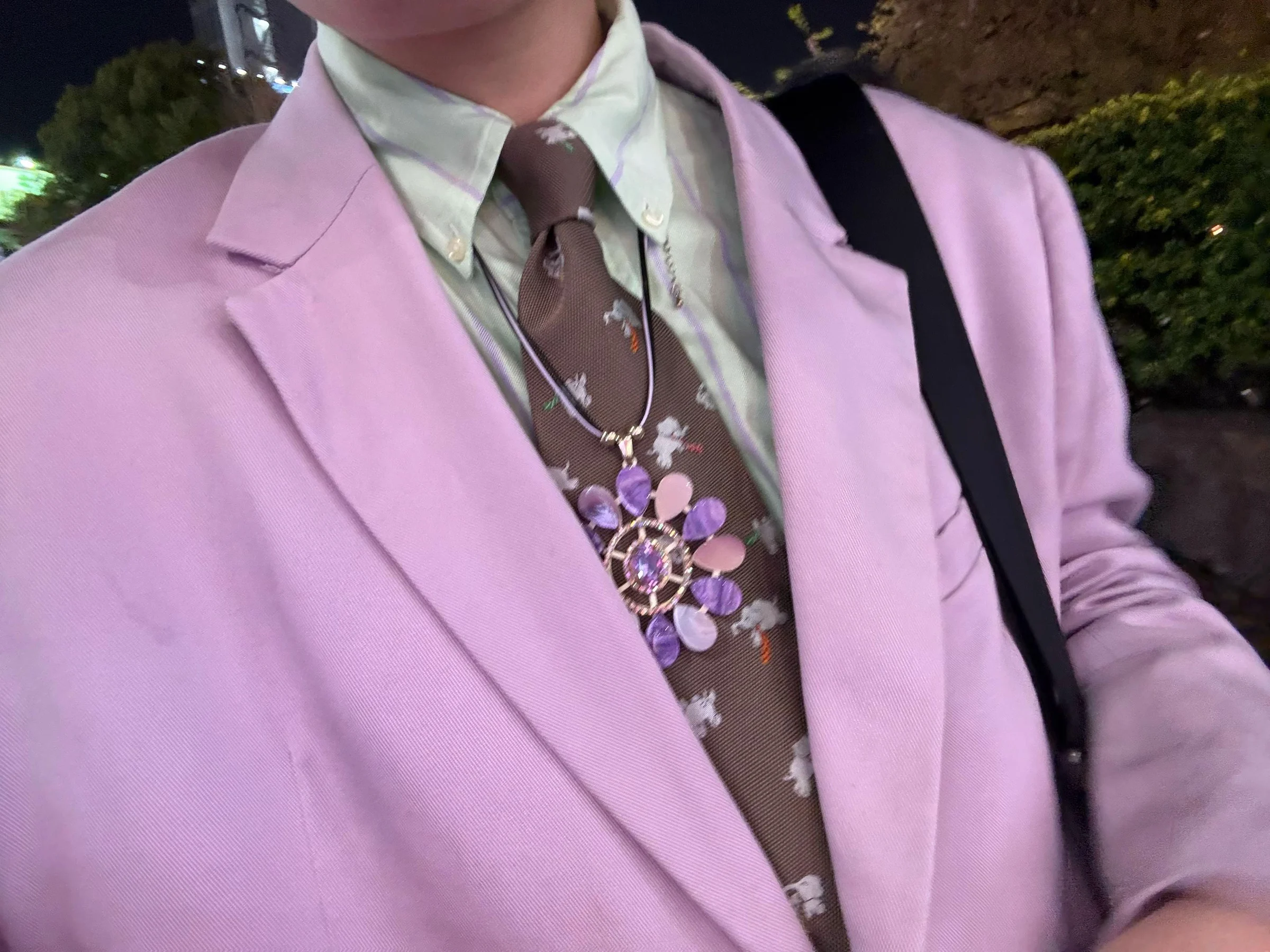 ピンクのジャケット、淡い緑のシャツ、茶色の花柄ネクタイを重ねた上半身のディテール