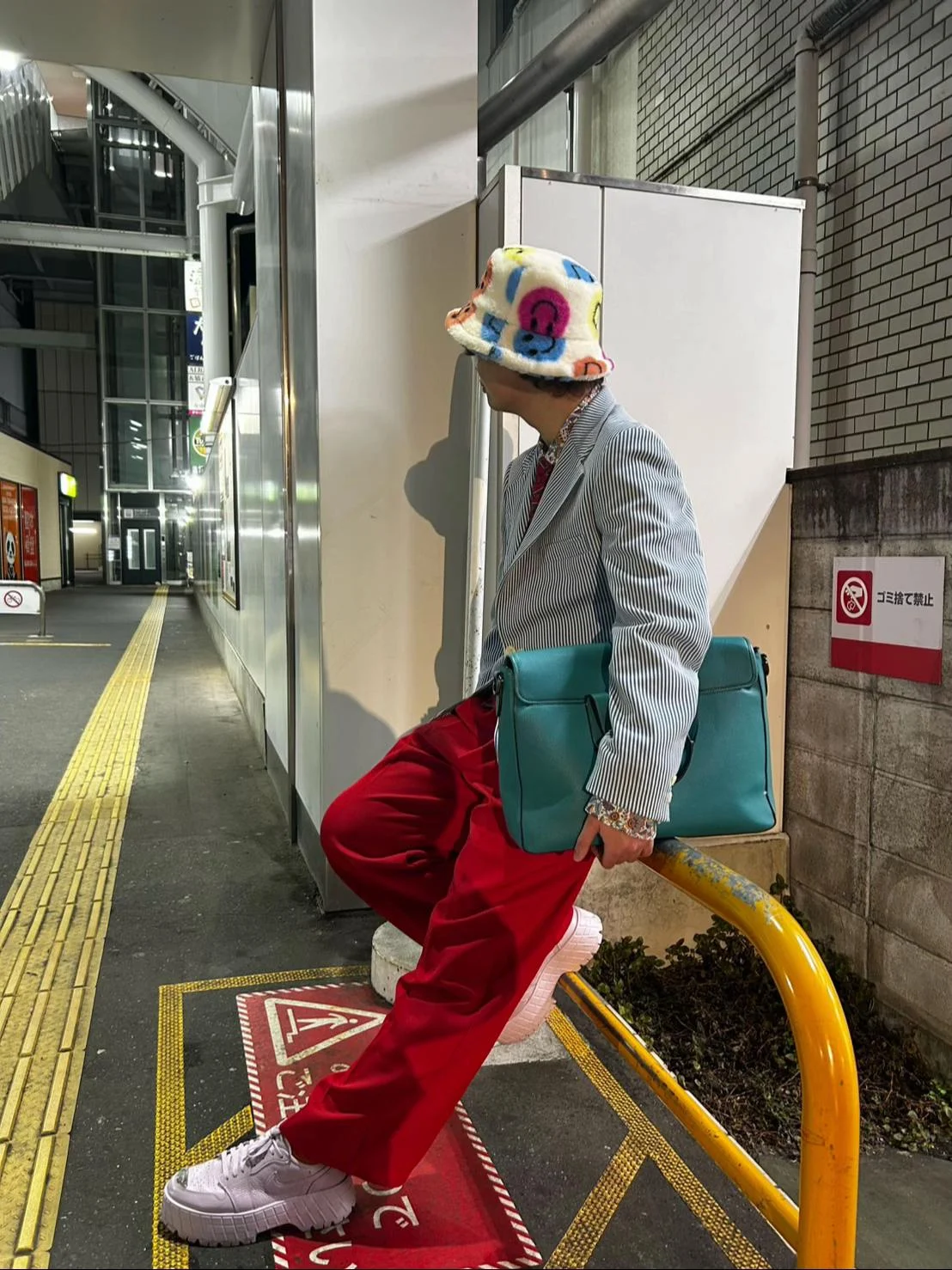 川崎の夜、青白ストライプジャケットに赤いワイドパンツ、ターコイズのバッグ、白い帽子と厚底靴を合わせた全身コーデ